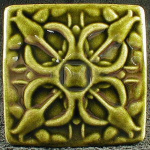 May include: A green ceramic tile with a raised, intricate design of overlapping, stylized leaves. The tile has a glossy finish and a square shape.