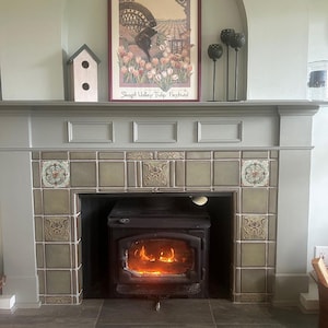 May include: A fireplace with a framed poster, a birdhouse, and decorative candle holders. The poster features a butterfly and tulips, with the text "Skagit Valley Tulip Festival." The fireplace has a lit fire inside.
