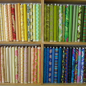 May include: A shelf filled with colorful fabric rolls, organized by color. The fabric rolls are arranged in rows, with each row featuring a different color scheme. The colors include red, orange, yellow, green, blue, and purple.