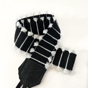 Peut inclure: Sangle de caméra rayée noire et blanche avec une frange blanche et une sangle réglable en cuir noir.