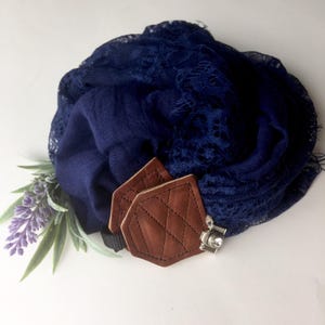 May include: A navy blue scarf with lace trim and a brown leather camera strap clip.