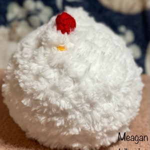 May include: White fluffy crocheted chicken with a red crocheted comb and a yellow beak.