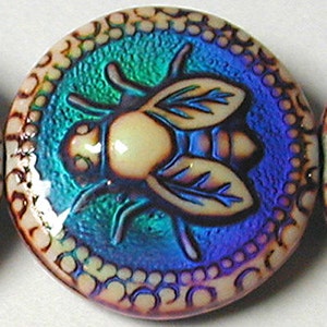 May include: A round, iridescent glass bead with a raised, white, embossed design of a fly. The bead has a blue, green, and purple iridescent finish.