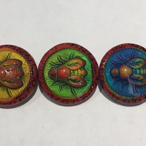 May include: Five round, red-rimmed, glass buttons with a raised, iridescent, green, blue, and yellow fly design.