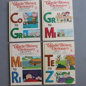 May include: Four colorful books with the title "The Charlie Brown Dictionary" by Charles M. Schulz. Each book features a different letter range and illustrations from the Peanuts comic strip. The books are numbered 2, 3, 4, and 6.