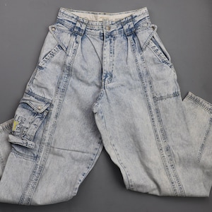 May include: Light blue denim cargo pants with a safety label on the left leg. The pants have a relaxed fit and multiple pockets.