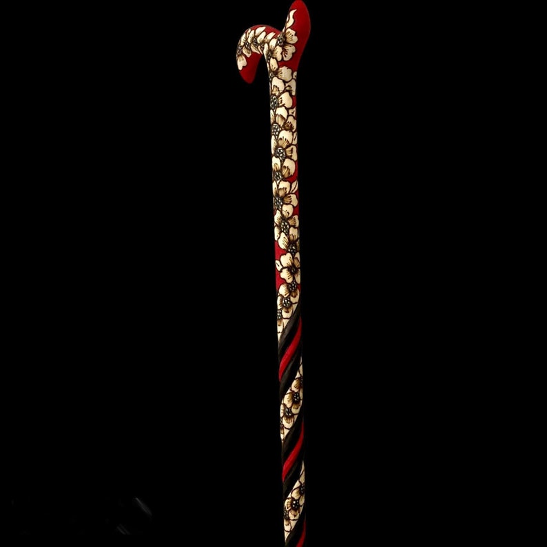 Puede incluir: Un bast&oacute;n de madera con un dise&ntilde;o de espiral rojo y negro y detalles florales blancos.