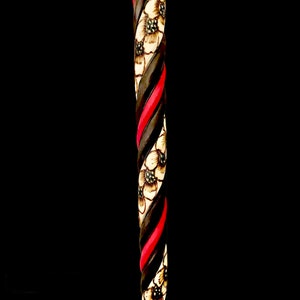Puede incluir: Un bast&oacute;n de madera con un dise&ntilde;o en espiral negro y rojo y flores blancas talladas en la madera.