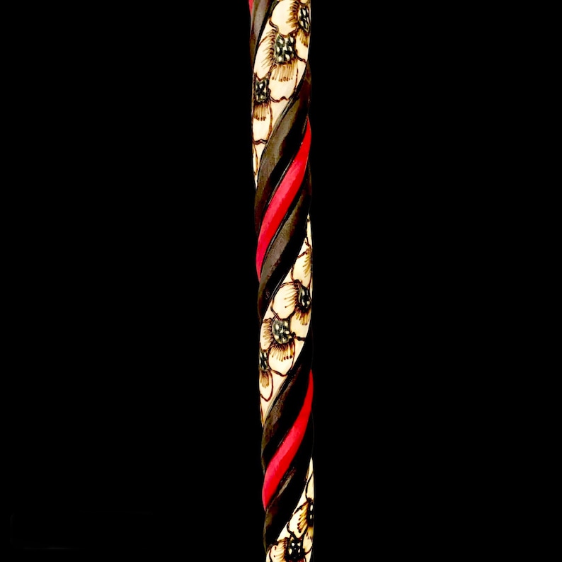 Puede incluir: Un bast&oacute;n de madera con un dise&ntilde;o en espiral negro y rojo y flores blancas talladas en la madera.