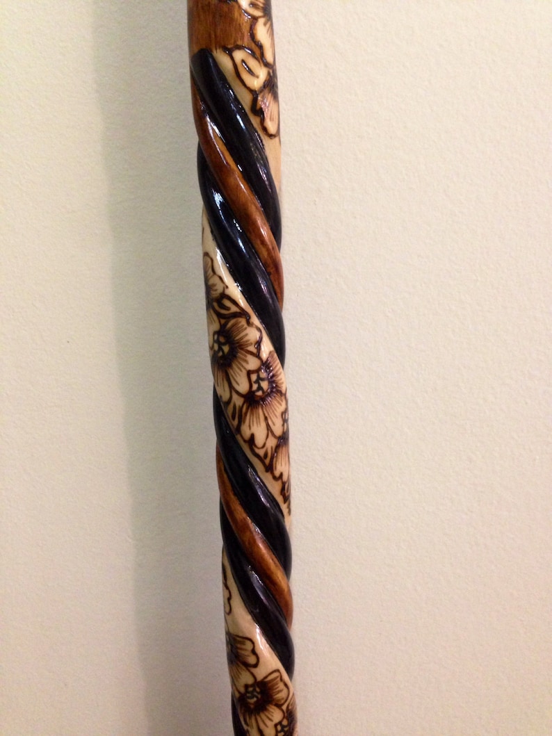 May include: A wooden walking stick with a black and brown spiral design and a floral pattern carved into the wood.