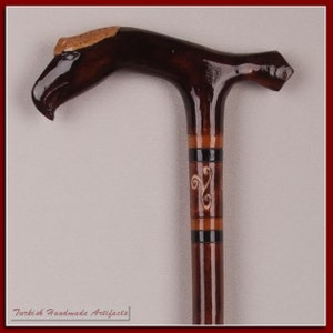 May include: A wooden walking stick with a carved eagle head handle. The stick is decorated with brown, black and white stripes and a carved design.