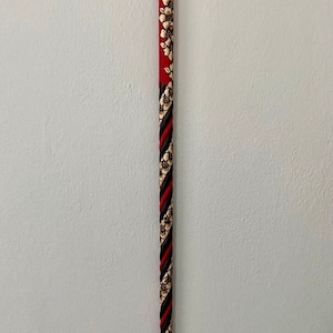 Puede incluir: Un bast&oacute;n rojo con un dise&ntilde;o floral en blanco y negro. El bast&oacute;n tiene un mango curvo y est&aacute; hecho de madera.