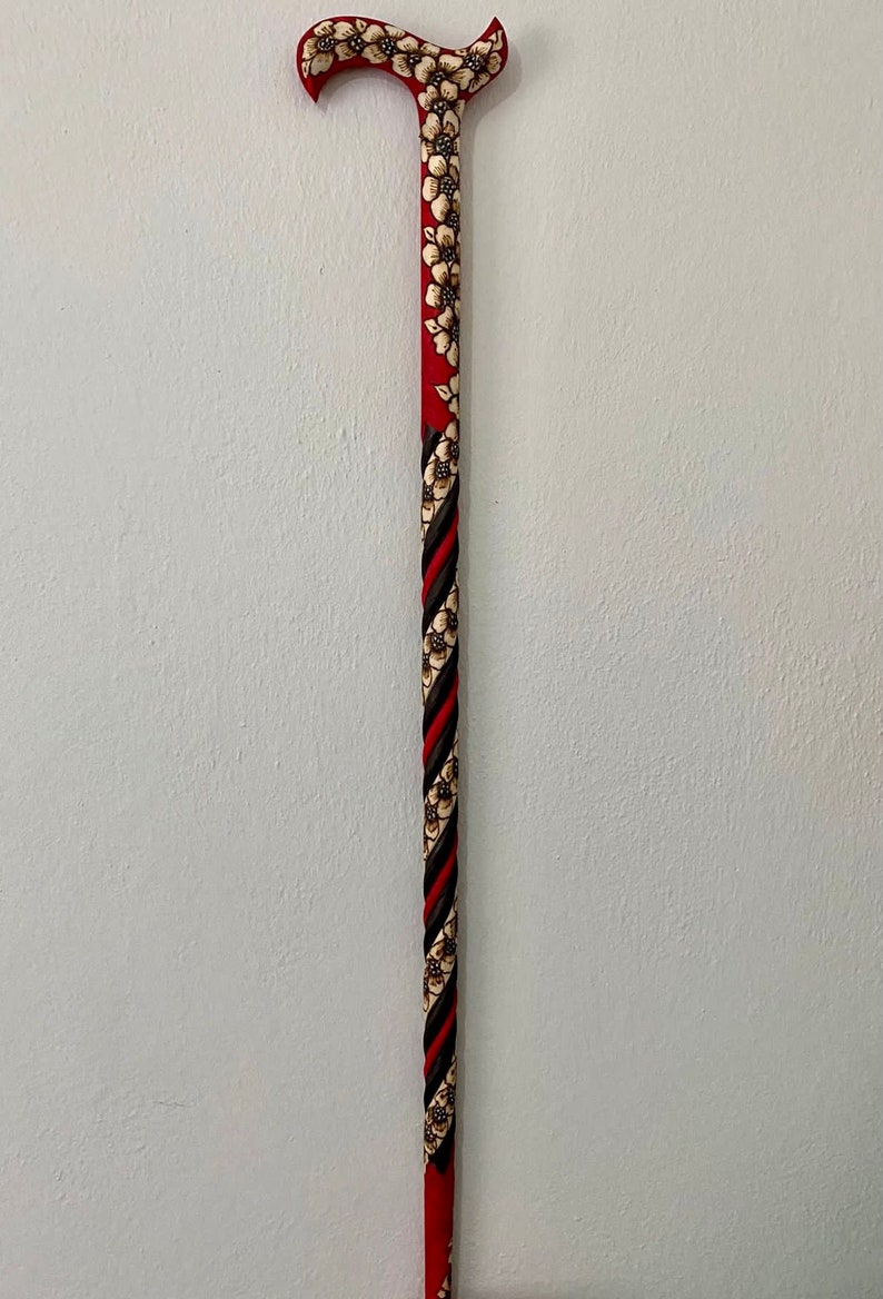 Puede incluir: Un bast&oacute;n rojo con un dise&ntilde;o floral en blanco y negro. El bast&oacute;n tiene un mango curvo y est&aacute; hecho de madera.