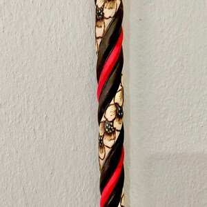 Puede incluir: Un bast&oacute;n de madera con un dise&ntilde;o retorcido. El bast&oacute;n est&aacute; pintado de negro y rojo con dise&ntilde;os florales blancos.