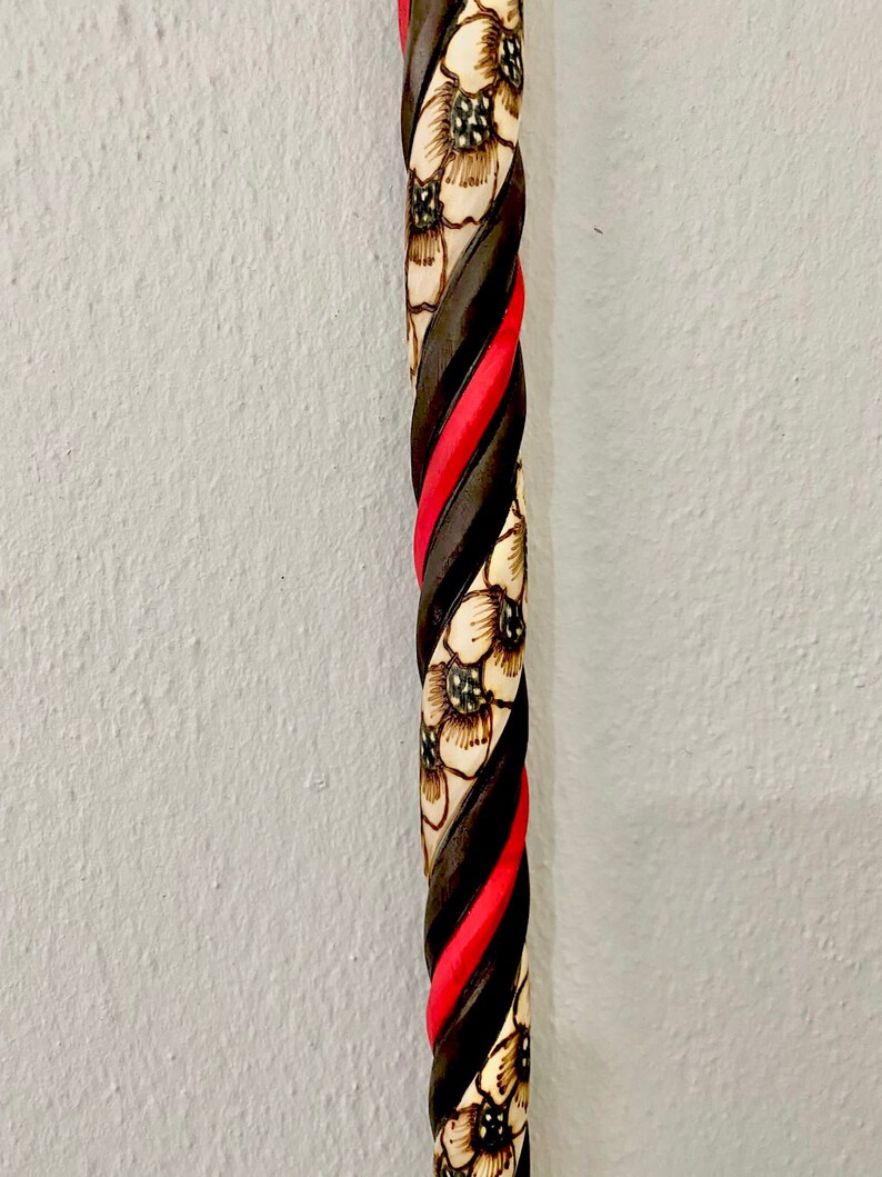 Puede incluir: Un bast&oacute;n de madera con un dise&ntilde;o retorcido. El bast&oacute;n est&aacute; pintado de negro y rojo con dise&ntilde;os florales blancos.