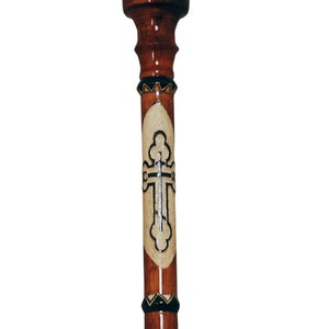 Peut inclure: Une canne de marche en bois avec une finition brune et un motif de croix décoratif. La croix est incrustée d'un matériau blanc et a un contour noir.