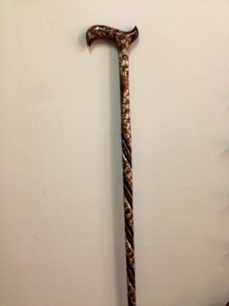 May include: A wooden walking stick with a carved design and a black and brown twisted shaft.