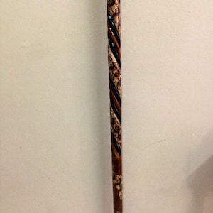May include: A wooden walking stick with a black and brown spiral design and floral carvings.