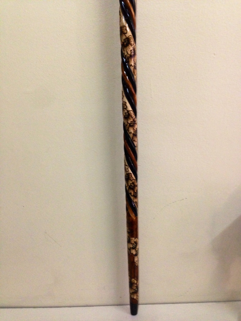 May include: A wooden walking stick with a black and brown spiral design and floral carvings.