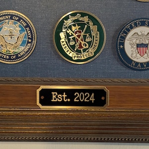 an example of a brass engraved plate being used on a picture frame to notate when something was established the item is a black rectangular plate with a gold border and gold text it also features two holes for mounting with small gold screws