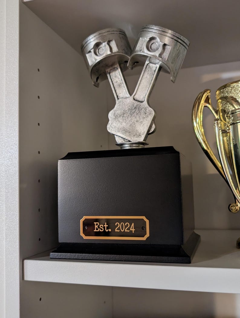 a black brass engraved tag shown in use on a trophy the tag is rectangular in shape with slightly notched corners a gold border and two holes for mounting