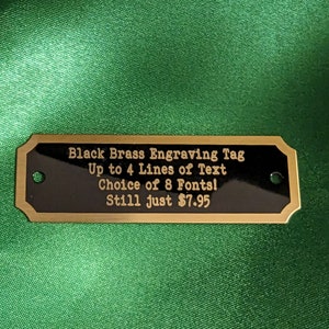 a brass engraving tag showing custom text that can be up to four lines they also offer eight different lettering choices and the price starts at just $7.95 the item is shown on a green satin background