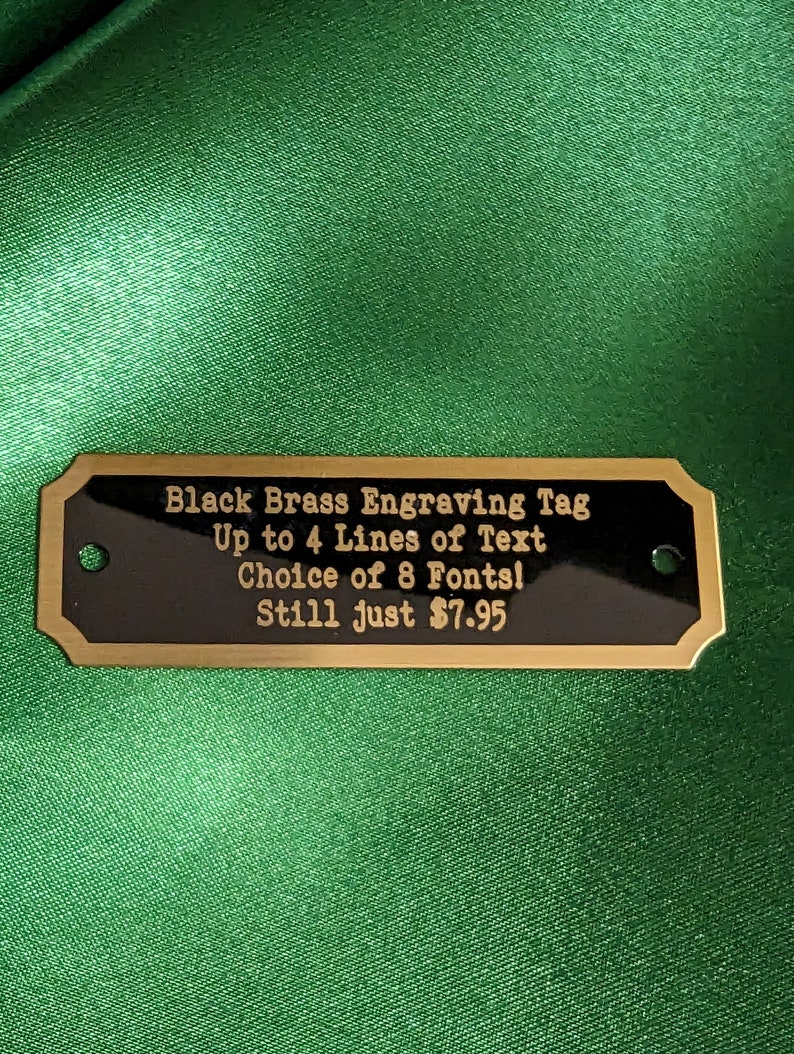 a brass engraving tag showing custom text that can be up to four lines they also offer eight different lettering choices and the price starts at just $7.95 the item is shown on a green satin background