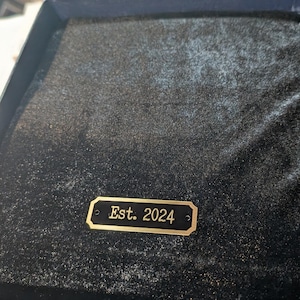 a personalized brass engraving plate shown with sample text on a Black Velvet background an example of it being used on a gift item