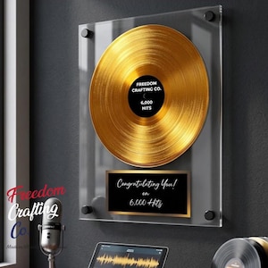 May include: A gold record mounted on a clear acrylic plaque with black hardware. The center label reads Freedom Crafting Co. 6,000 Hits. A black plaque below features the text Congratulating You! on 6,000 Hits in white script and print lettering.