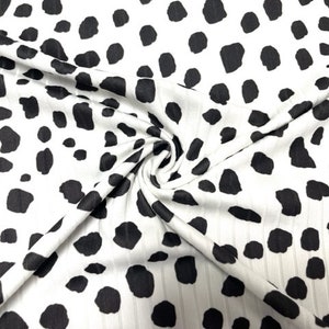 May include: White fabric with a black dalmatian print. The fabric has a ribbed texture.