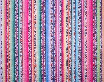 May include: A vibrant fabric with vertical stripes in various colors, including pink, green, blue, and orange. Some stripes feature a leopard print pattern. The overall design is colorful and eye-catching, suitable for clothing or home decor.