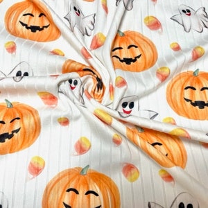 May include: White fabric with a repeating pattern of orange pumpkins with smiling faces, white ghosts, and yellow and orange candy corn.