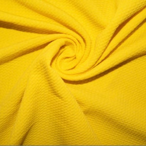 Puede incluir: Primer plano de una tela de punto de waffle amarilla. La tela es suave y texturizada, con un brillo sutil.