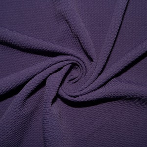 Puede incluir: Tela de punto de waffle morado con una superficie texturizada. La tela está doblada y retorcida, mostrando la textura y el drapeado.