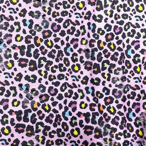 May include: Close-up of a pink fabric with a leopard print design. The black spots are filled with various colors, including yellow, orange, blue, and purple. The fabric has a distressed, torn appearance.