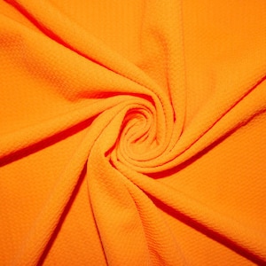 May include: Close-up of a bright orange fabric with a textured surface. The fabric is folded and twisted, creating a swirling pattern.