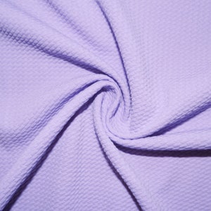 Puede incluir: Primer plano de un remolino de tela morada clara con una superficie texturizada y con hoyuelos. La tela está fuertemente arremolinada, creando un patrón de pliegues y sombras. El material parece suave y flexible, adecuado para ropa o manualidades.