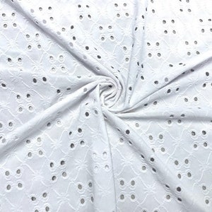 May include: White eyelet fabric with a repeating floral and dot pattern. The fabric is folded and draped, showing the texture and design. The eyelet holes are evenly spaced throughout the fabric.