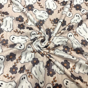 May include: A beige fabric with a repeating pattern of white ghosts and brown flowers. The fabric has a subtle texture.