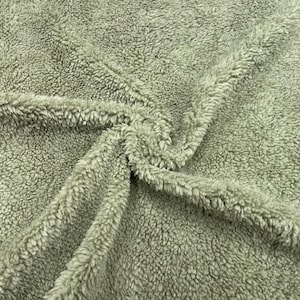 Puede incluir: Primer plano de una tela verde salvia, afelpada, con una superficie texturizada y difusa. La tela está doblada y drapeada, mostrando el pelo suave y denso. El material parece cálido y acogedor, adecuado para mantas o prendas.