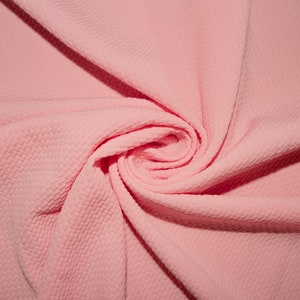 Puede incluir: Primer plano de una tela texturizada rosa. La tela está doblada y retorcida, creando un patrón en espiral.