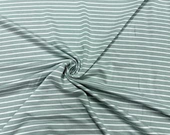 Puede incluir: Primer plano de una tela con rayas horizontales. La tela es de color verde apagado con rayas blancas. La tela está doblada y arremolinada, mostrando la textura y el patrón del material.