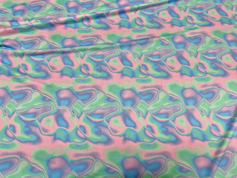 May include: Fabric with a wavy, abstract pattern in pastel colours. The design features flowing shapes in shades of pink, blue, and green, creating a soft, iridescent effect. The fabric appears to be lightweight and flowing.