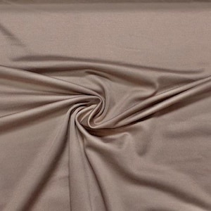 Pode incluir: Close-up de um tecido com um padrão em espiral. O tecido é de cor castanha lisa e suave com um ligeiro brilho. As dobras e vincos criam sombras e destaques, adicionando profundidade e textura ao material. Adequado para vestuário e decoração de casa.