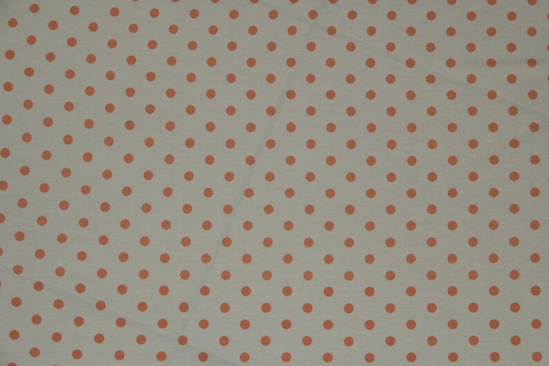 May include: A white fabric with a repeating pattern of small orange polka dots.