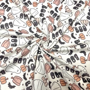 May include: White fabric with a repeating Halloween pattern. The design includes ghosts, pumpkins, bats, stars, and the word "BOO" in black. The pumpkins are peach-colored, and the ghosts are white.