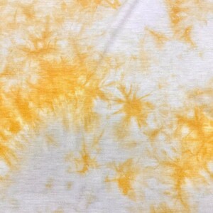 May include: A white fabric with a tie-dye pattern in shades of yellow. The fabric has a soft, textured surface.