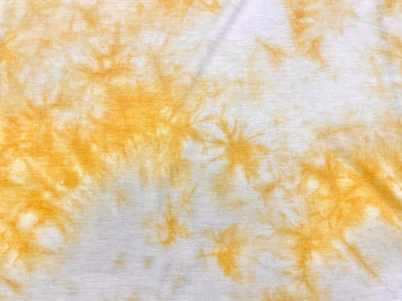 May include: A white fabric with a tie-dye pattern in shades of yellow. The fabric has a soft, textured surface.