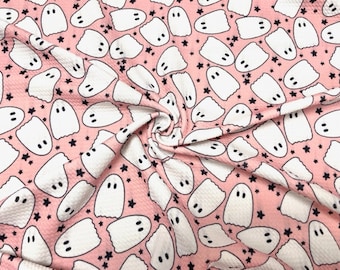May include: Pink fabric featuring a repeating pattern of white cartoon ghosts and black stars. The ghosts have simple, oval eyes and a curved mouth. The fabric has a textured appearance.