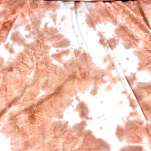 May include: A white fabric with a tie-dye pattern in shades of peach and brown.